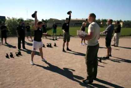 A group kettlebell class training outdoors with kettlebells lined up on the ground